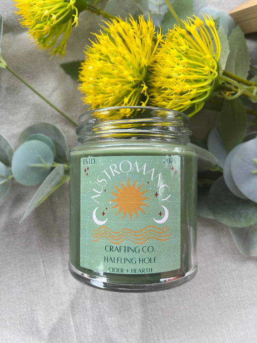 A Halfling Hole candle, on a table with dandelions and greenery.