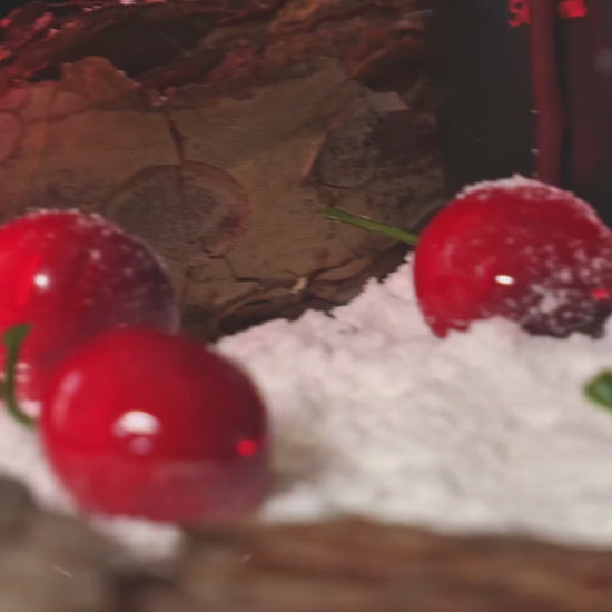 The Cherry and hibiscus mead is sat in a snowy landscape, with cherries scattered around it. The mead is poured into a fancy cup, with more sweeping shots of the bottle and scenery.